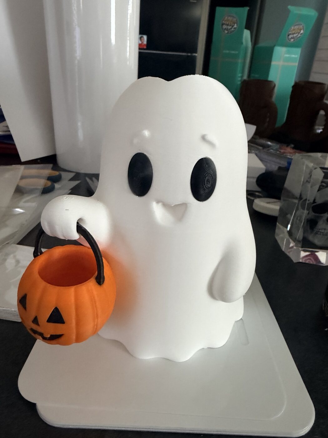 White ghost character holding an orange pumpkin candy bucket