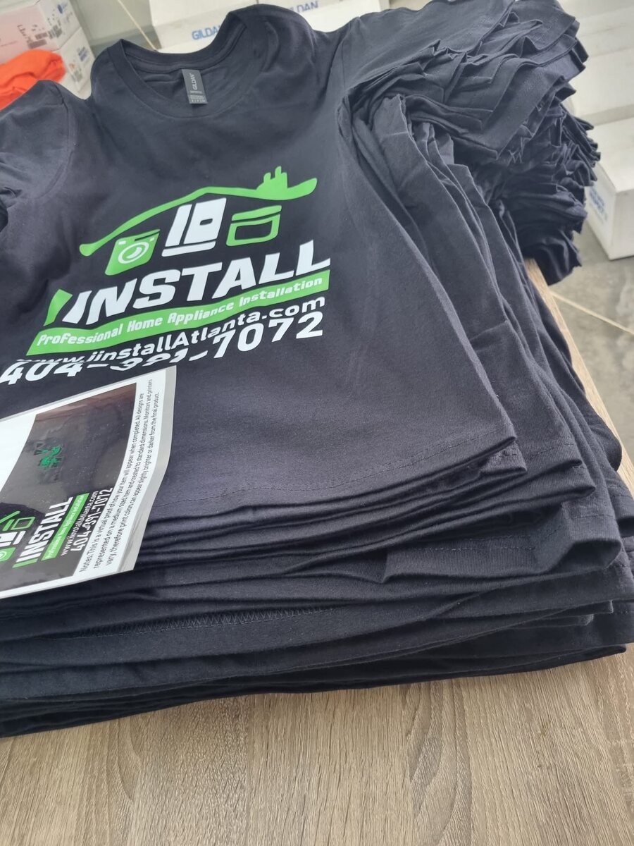 Stack of custom black company T-shirts with green and white printing