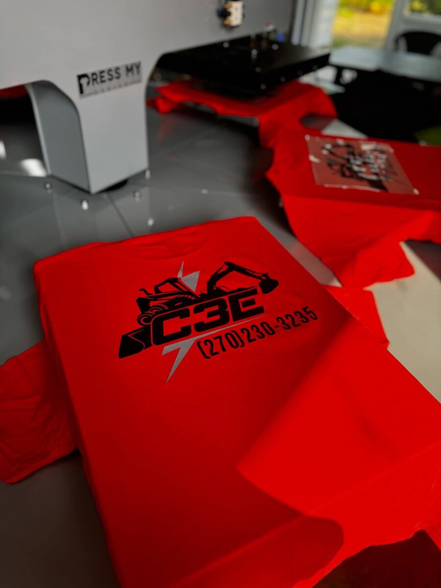 Red custom construction company shirts being printed in the shop